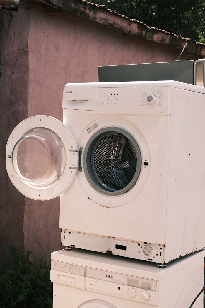 Outdoor view of two stacked laundry machines with an open door, showing rustic surroundings.